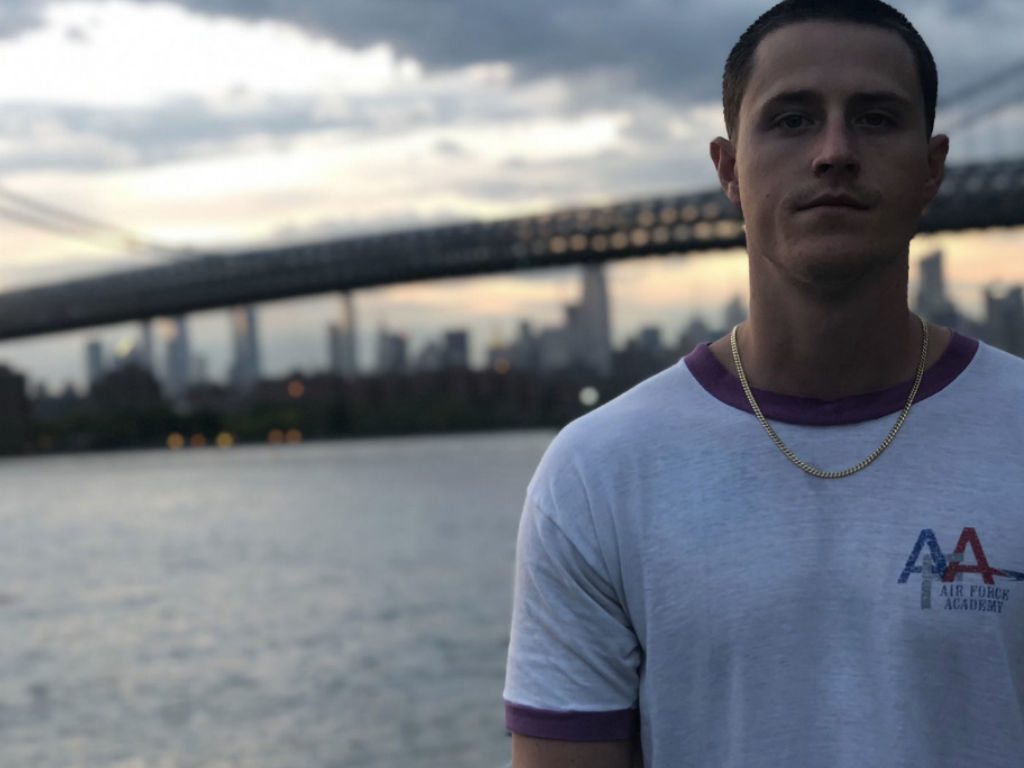 Shane Harper looking into the camera while standing in front of the Brooklyn Bridge.