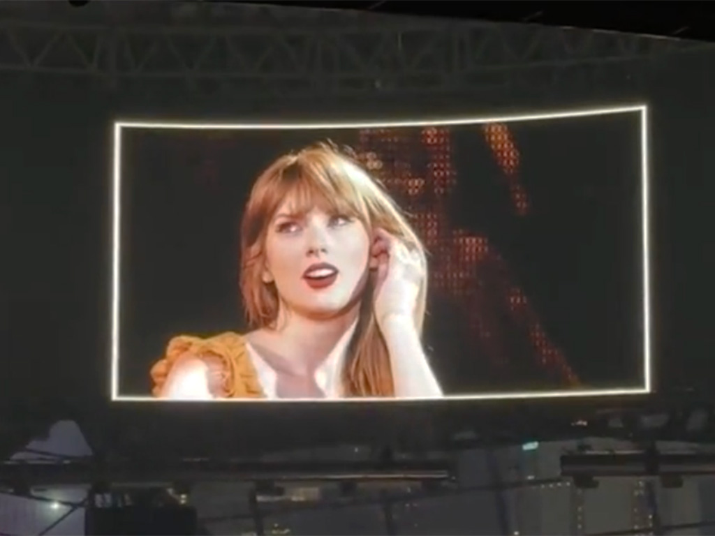 Taylor Swift performing in concert, wearing a yellow dress and red lipstick.