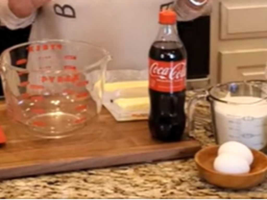 A woman standing behind cooking ingredients, including eggs, butter, sugar and Coca-Cola