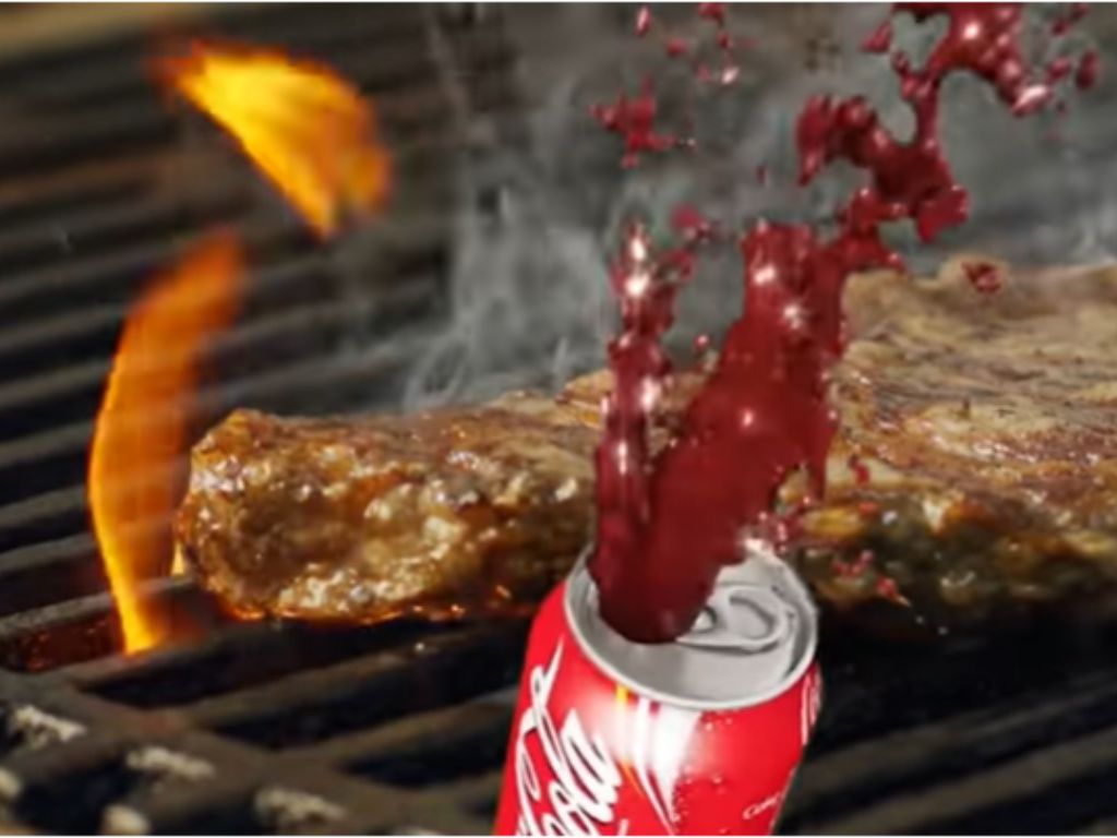 Coca Cola being poured on meat cooking on a grill