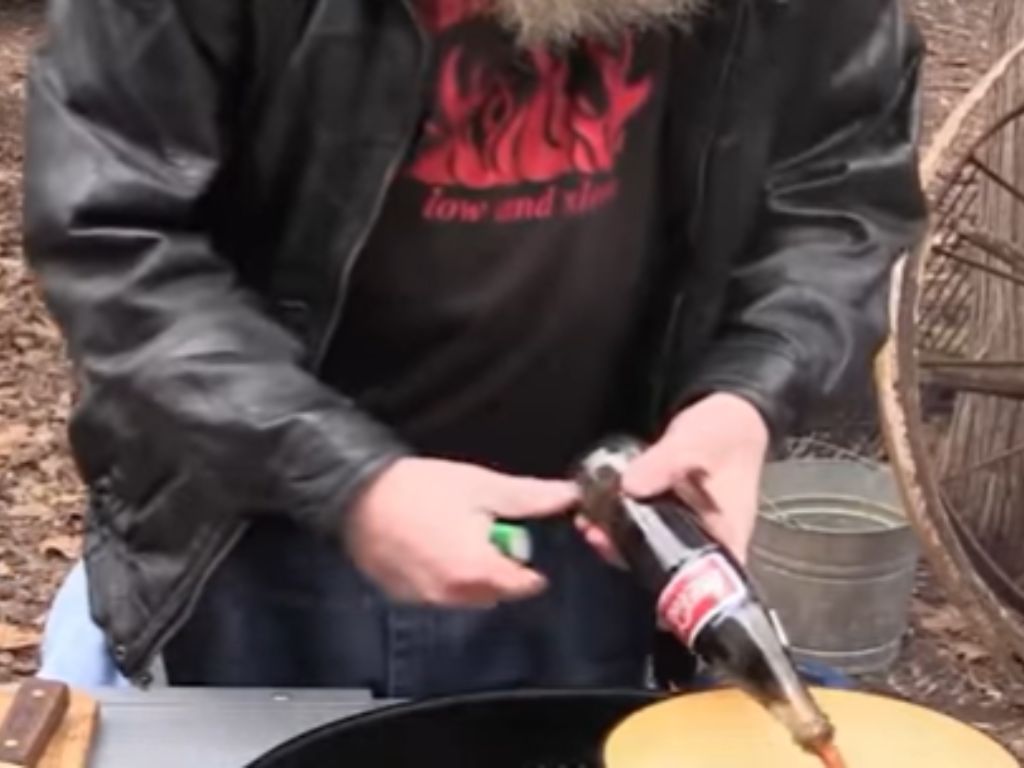 A bottle of Coca Cola being poured into a cooking pan