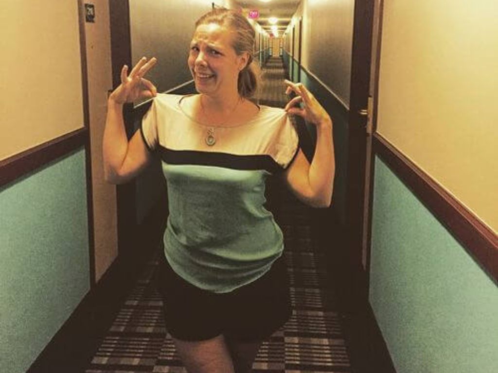 A woman wearing a shirt that matches the colors of the walls in a hotel hallway 