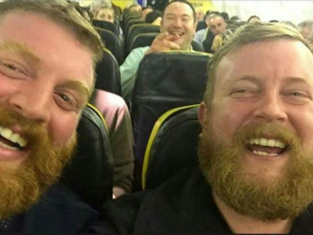 Two men who look alike laughing on a plane