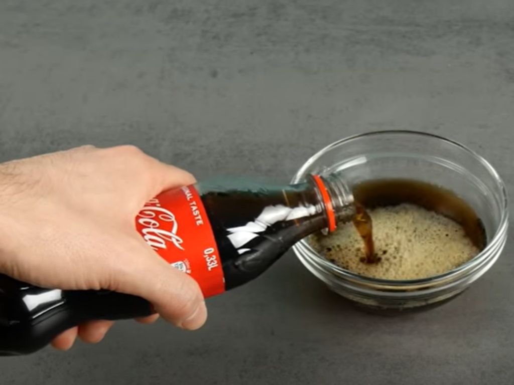 A bottle of Coca Cola being poured into a bowl