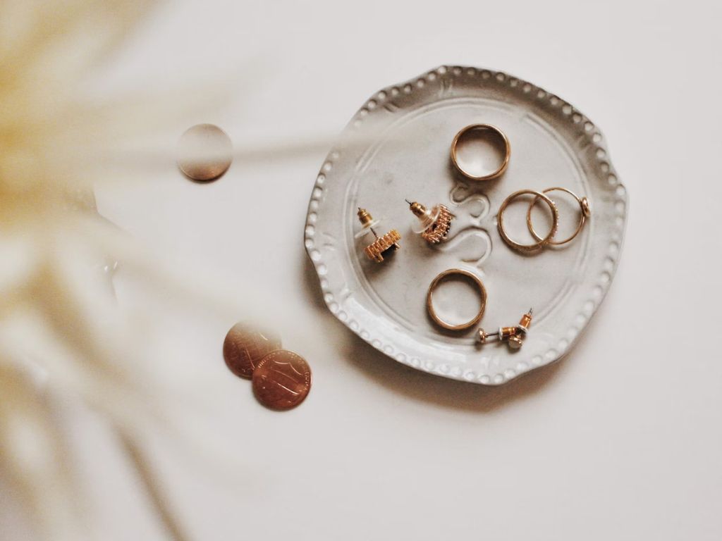 A jewelry holder filled with earrings, rings and some coins