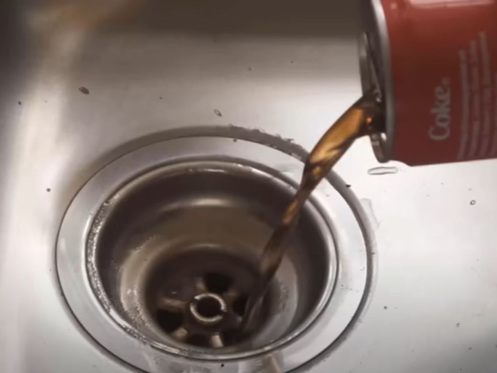 Coca Cola being poured down a sink drain