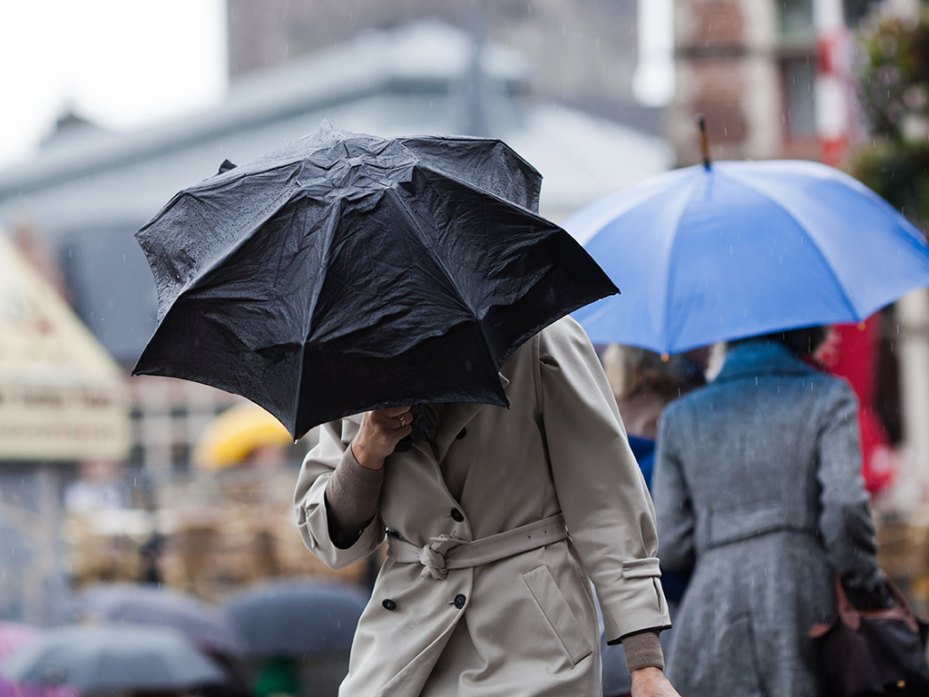 A person in a trench coat holding an umbrella while it rains outside.