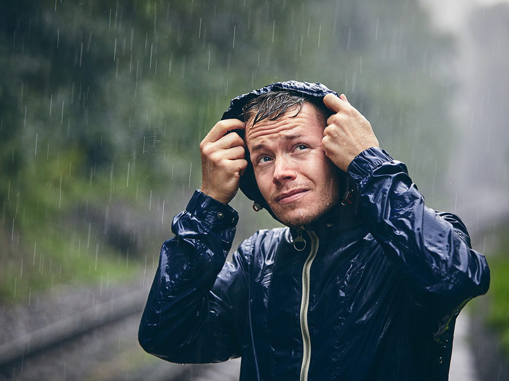 A man in a hoodie looking up in the rain.