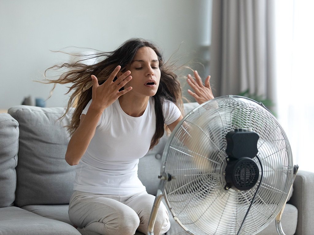 A woman waving her hands while sitting in front of a fan