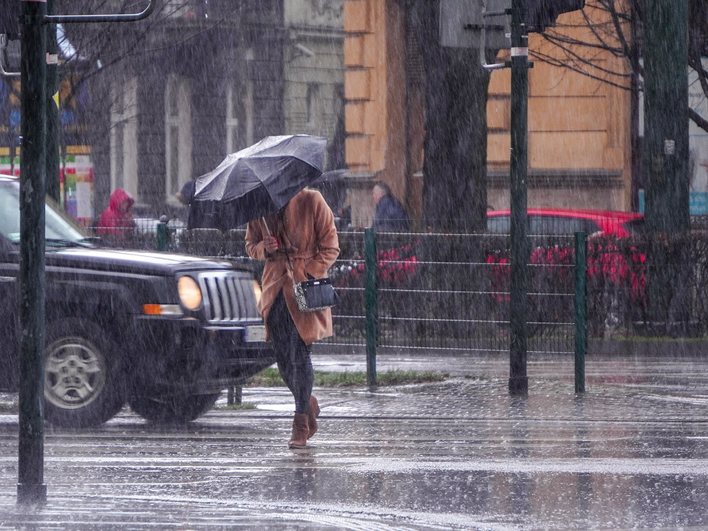 A woman walking in the rain while wearing a brown coat.