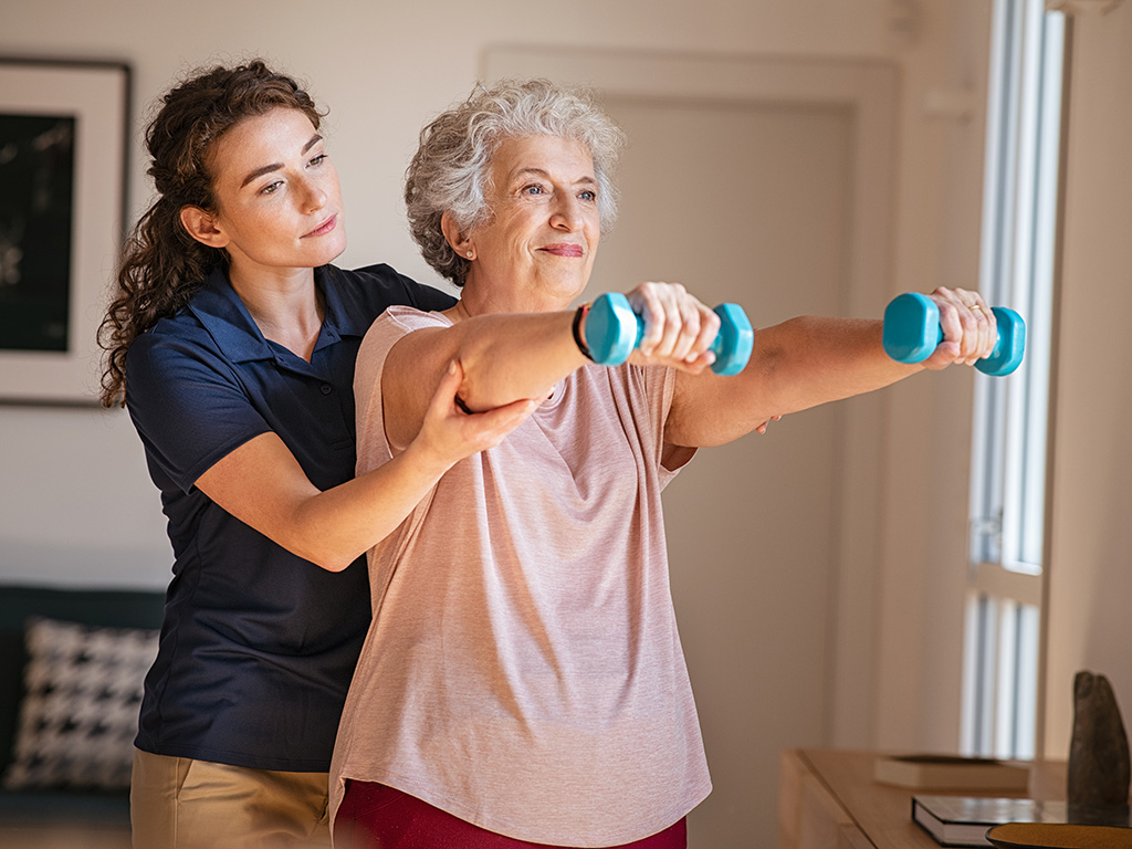 A physical therapist helping an elderly woman lift weights