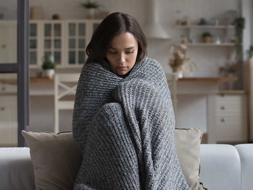 A cold woman huddling in a blanket on a couch.