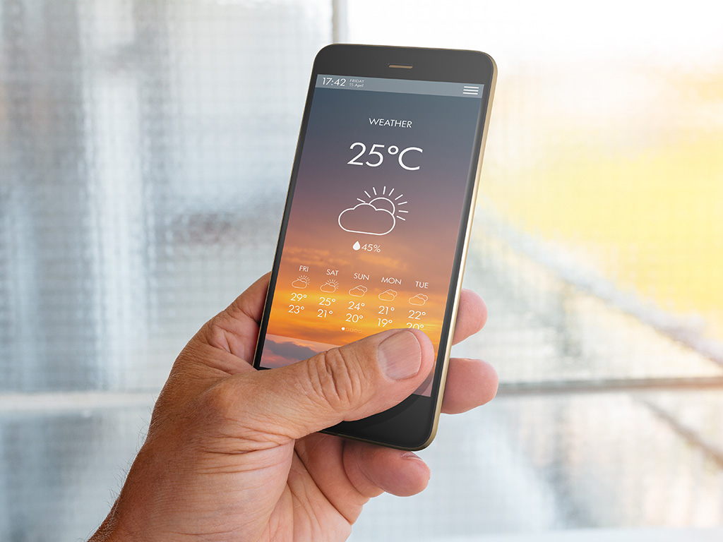 A hand holding a smart phone that shows a weather report