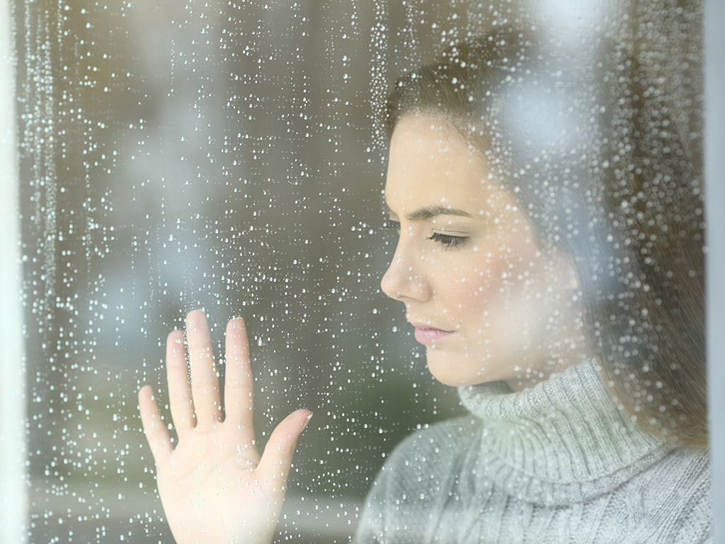 A woman holding her hand up to a window during a rain storm.