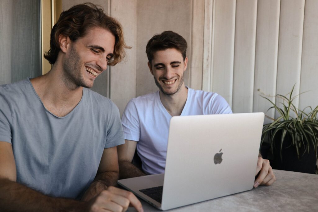 Two adult men smiling at a laptop screen