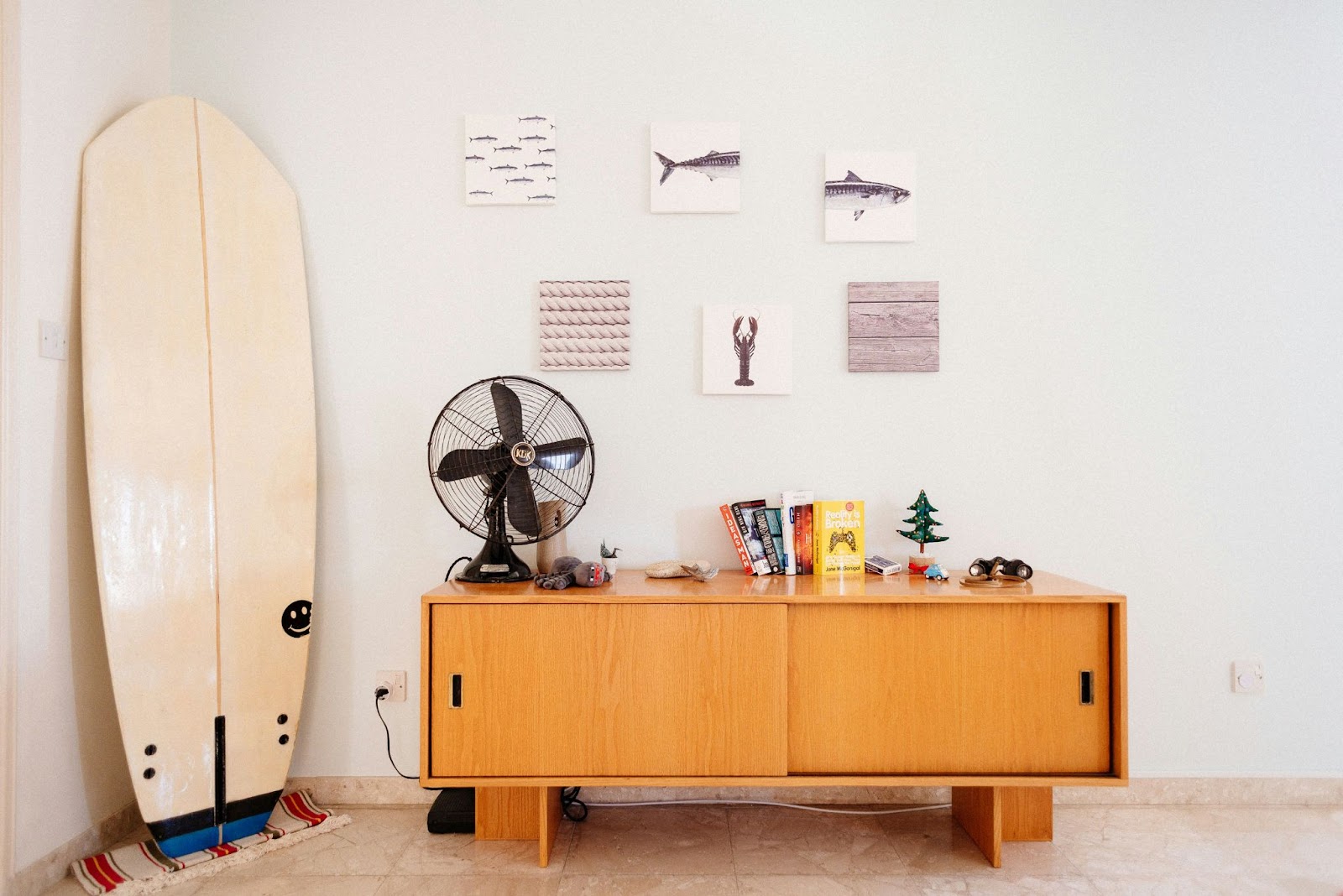 A room with a side table, fan and surfboard 