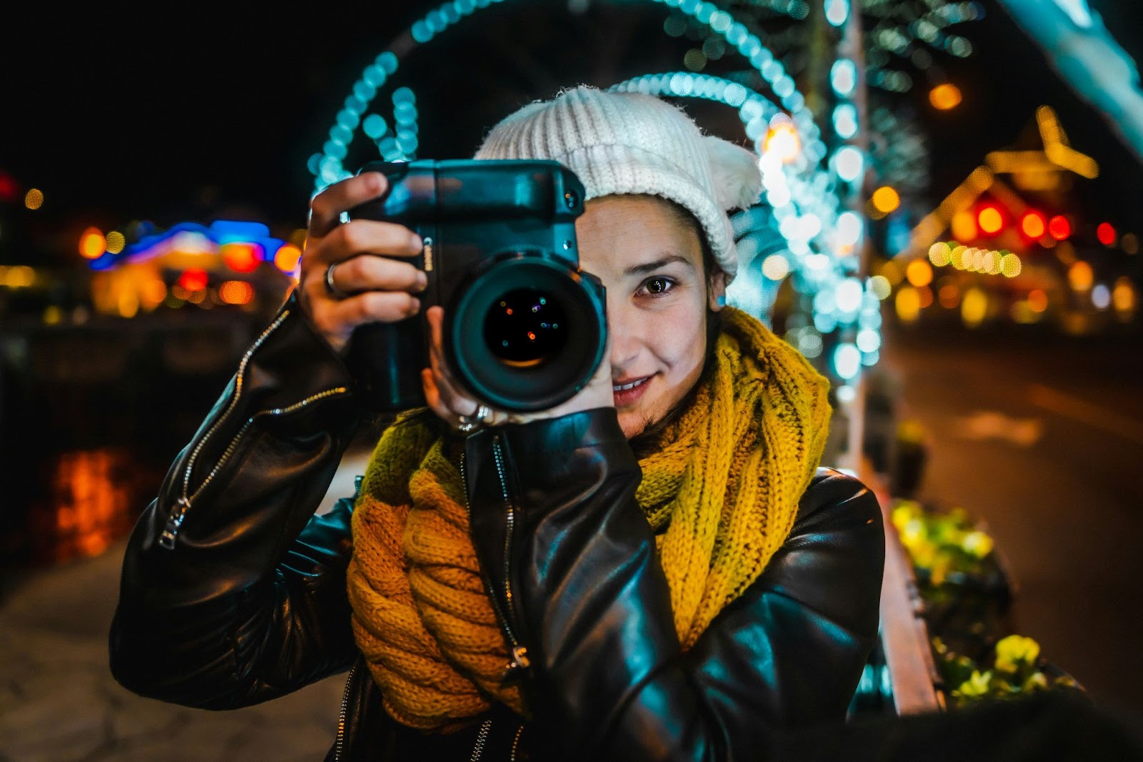 A woman in a hat and scarf taking a photo with a camera