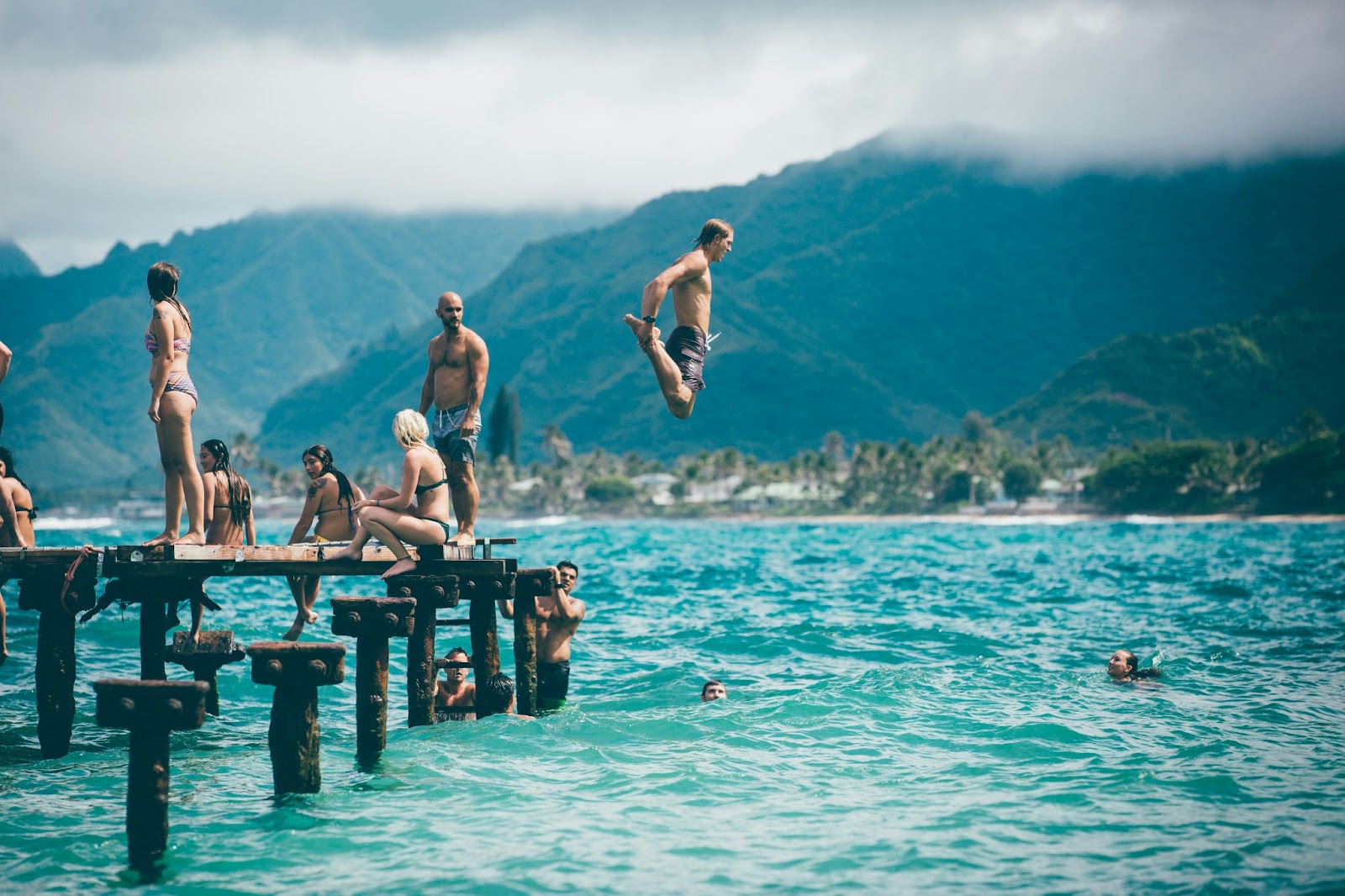 People diving into a body of water in front of a mountain landscape