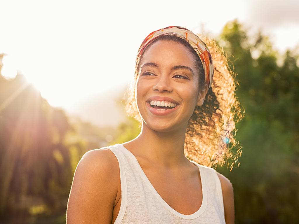 Portrait of beautiful african american woman smiling and looking away at park during sunset. 