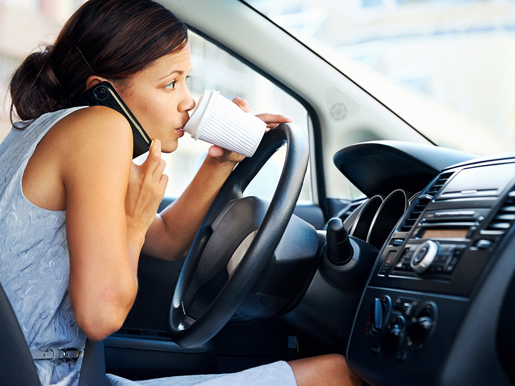 Young woman driving while talking on the phone and drinking coffee