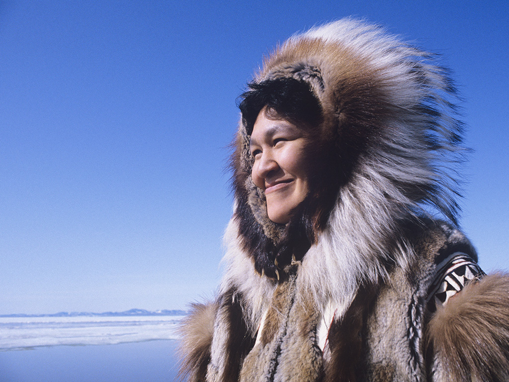 Smiling Eskimo woman wearing traditional clothing in wind against clear blue sky