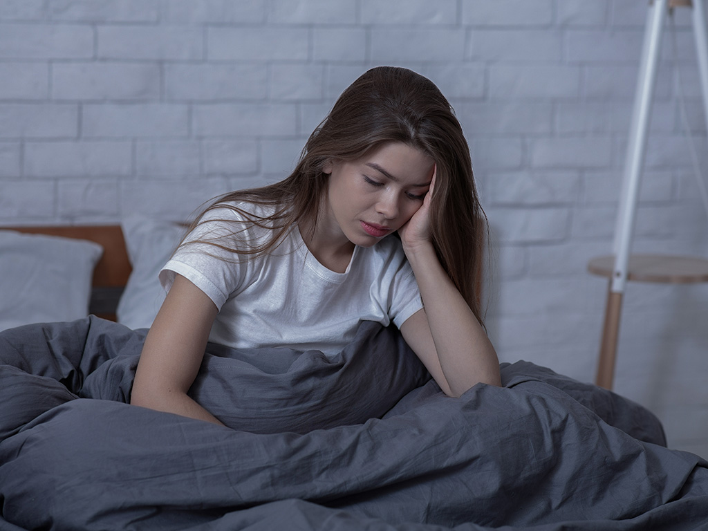 Sad young woman with seasonal affective disorder or depression sitting alone in her bed.