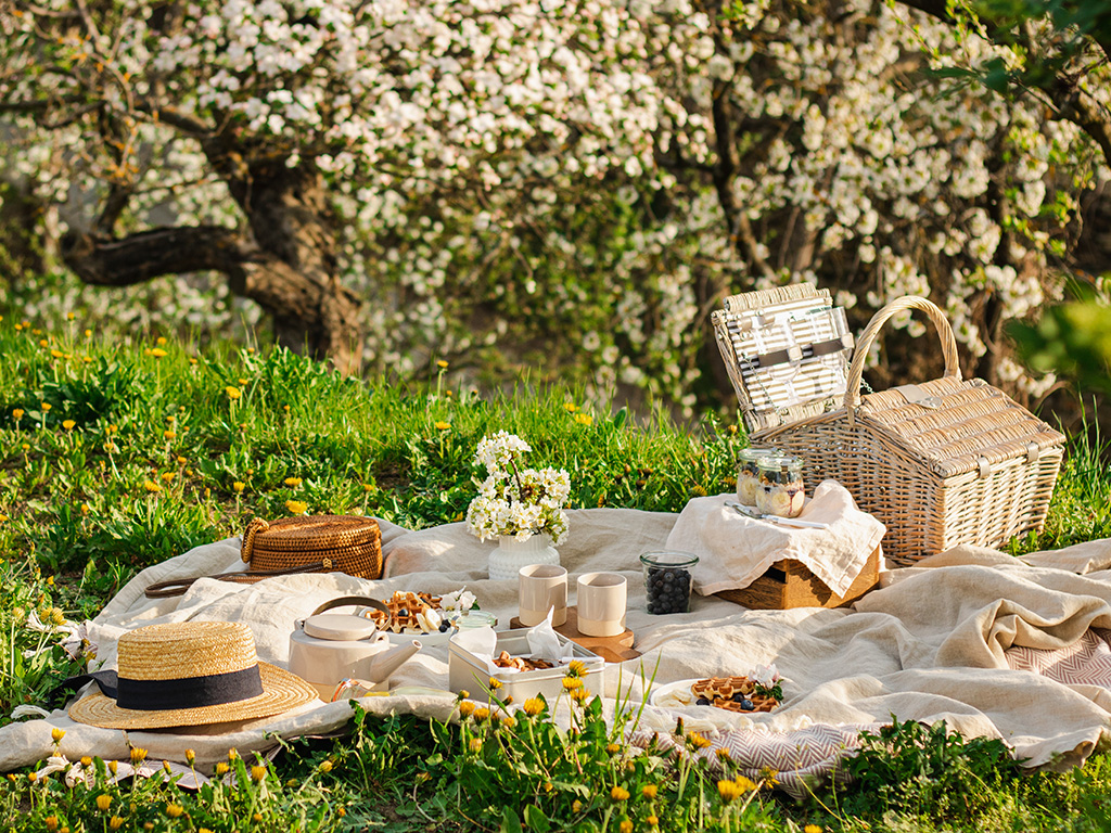 A picnic with baskets, food and drink and a white blanket