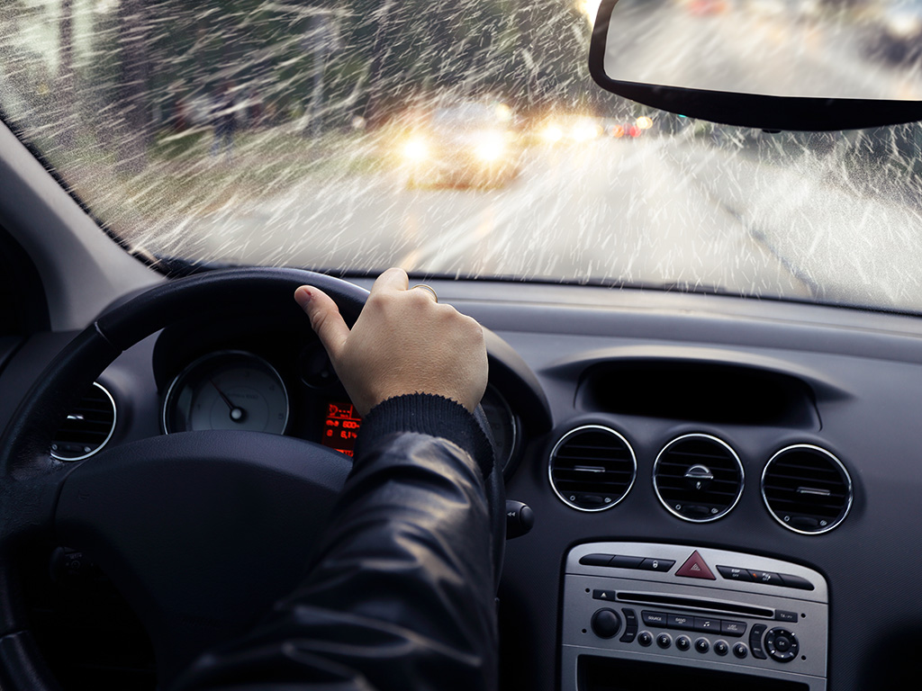 A person driving in a rainstorm with one hand on the wheel