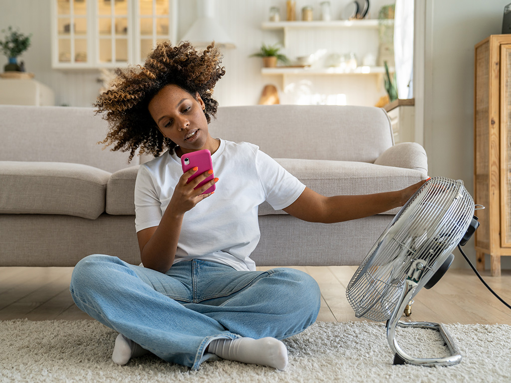 A woman sitting in front of a fan and looking at her phone