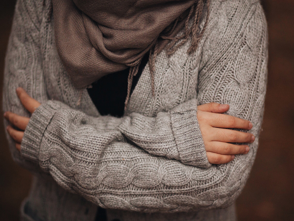 Person wearing a sweater and scarf and hugging themself