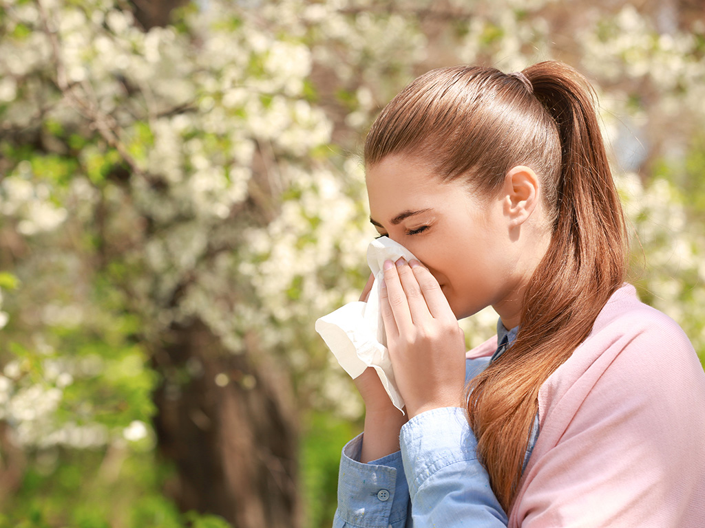 A woman sneezing in front of flowers