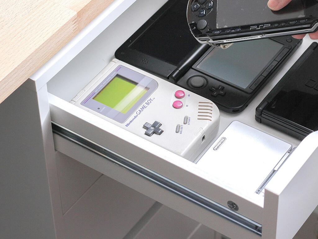 Open desk drawer with retro hand held gaming consoles. 