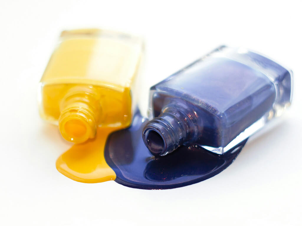 Yellow and purple bottles with pouring nail polish.