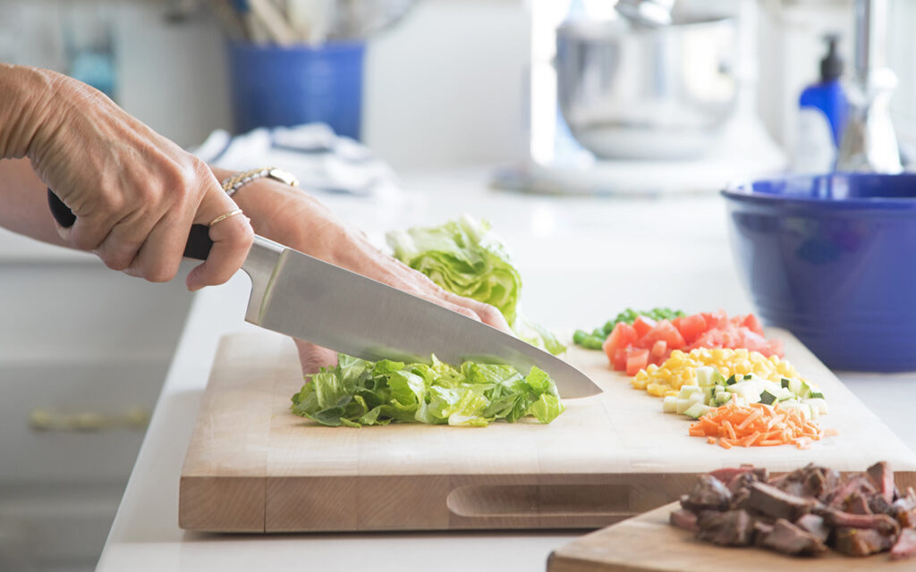 Photograph of a woman's hand cutting up vegetable for a salad