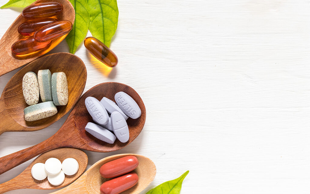 Variety of vitamin pills in wooden spoon on white background with green leaf