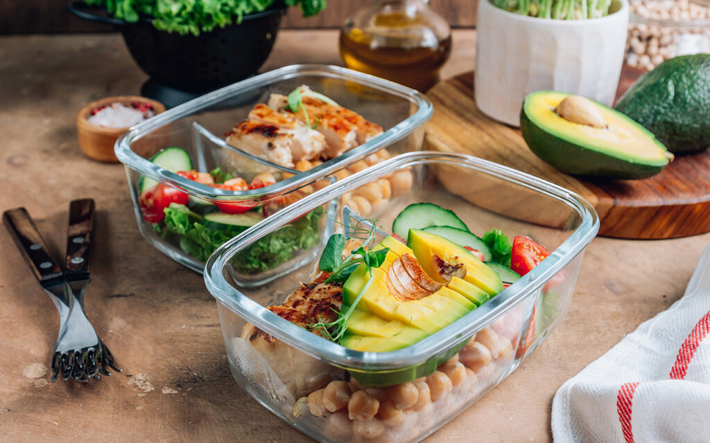 Healthy meal prep containers with chickpeas, chicken, tomatoes, cucumbers and avocados. 