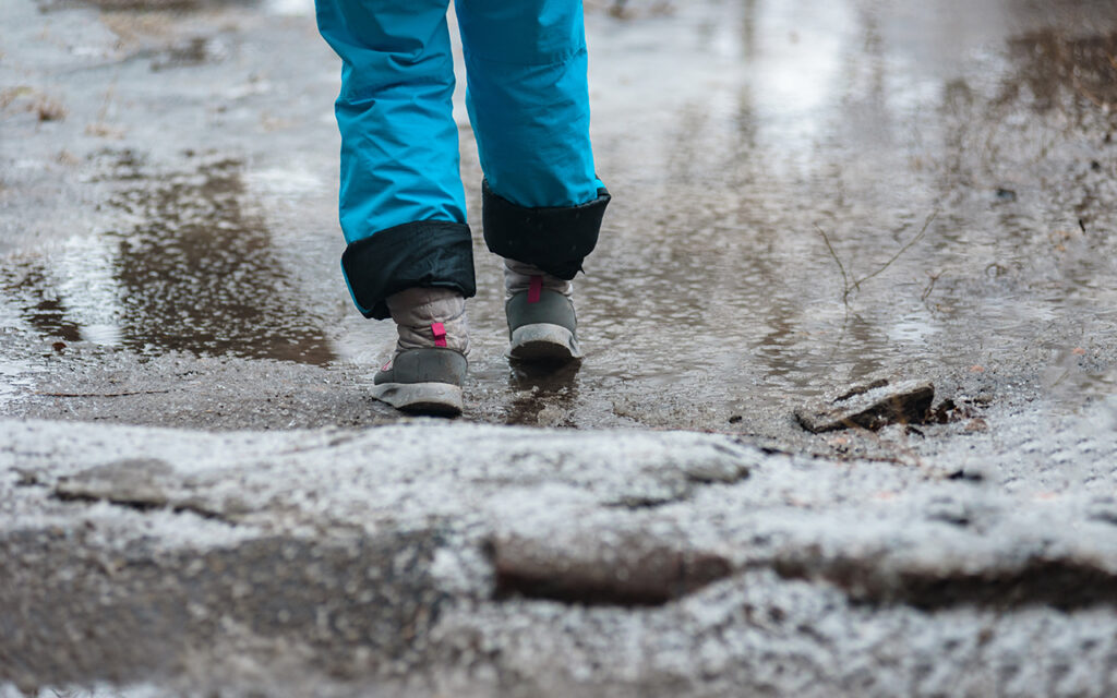 Person in warm shoes standing on wet winter road